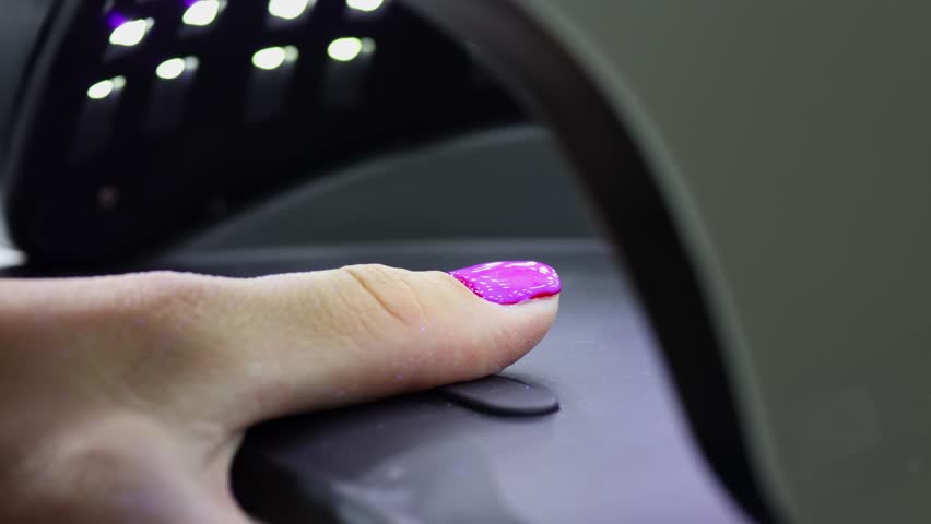 UV Lamp Curing Gel Polish on Thumb Nail, Close-up video of a thumb with pink gel polish under a UV lamp during the nail curing process at a beauty salon.
