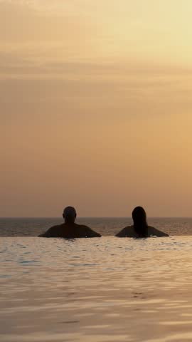 Silhouettes, couple in love, man and woman, relaxing in water, on edge of outdoor infinity pool with panoramic sea view, at sunrise. honeymoon, travel and vacation concept