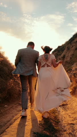A young couple walks towards the sun between two mountains. Happy people holding hands and walking in front to the sun. Silhouette of a man and a woman on the counter sun. Time together.