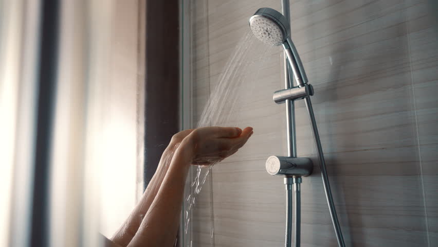 Young woman taking shower in modern glass shower cabin and wash face. Girl washing under running water in hotel or at home.