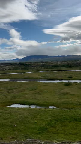 A tranquil Icelandic scene with green fields, rivers, and mountains under a partly cloudy sky, tc01
