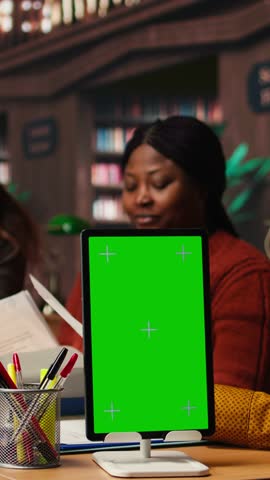 Vertical Video Mature colleagues team review paperwork next to chroma key mockup, using multiple academic sources and books in classic library setting. Learning space with library resources. Camera A.