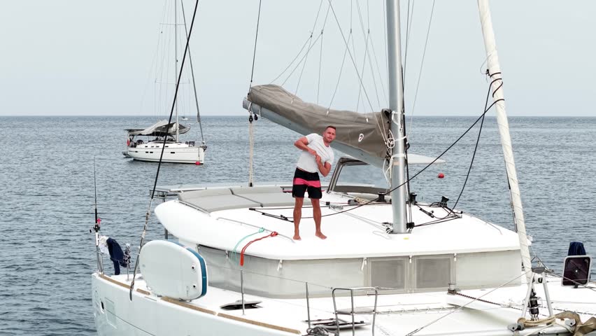 Morning on a yacht. Fitness exercises on the roof of a catamaran. A man doing exercises during a sea voyage. Warm-up exercises, morning activity.