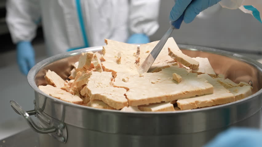 Close-up of pharmaceutical factory workers in sterile uniforms and gloves filling raw vitamin or drug ingredients into sterile containers during production process.