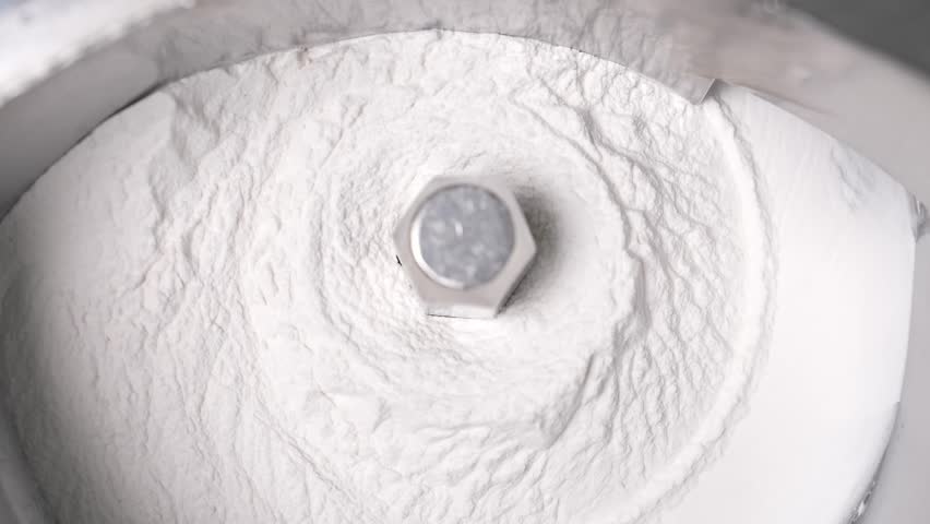 Close-up of a stainless steel pharmaceutical machine mixing white powder raw material for medicine or vitamin production in a cleanroom environment.