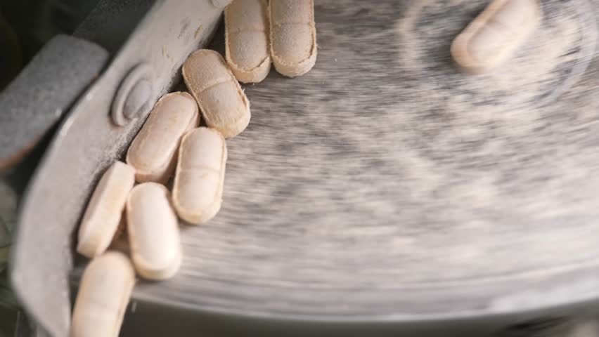 Close-up of compressed medicine or vitamin tablets falling and colliding gently as they exit the pharmaceutical press machine in a cleanroom facility.