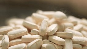 Close-up shot of medicine or vitamin tablets falling toward the camera in slow motion inside a clean pharmaceutical manufacturing facility. - Powered by Shutterstock - Get 15% off with code: PIKWIZARD15