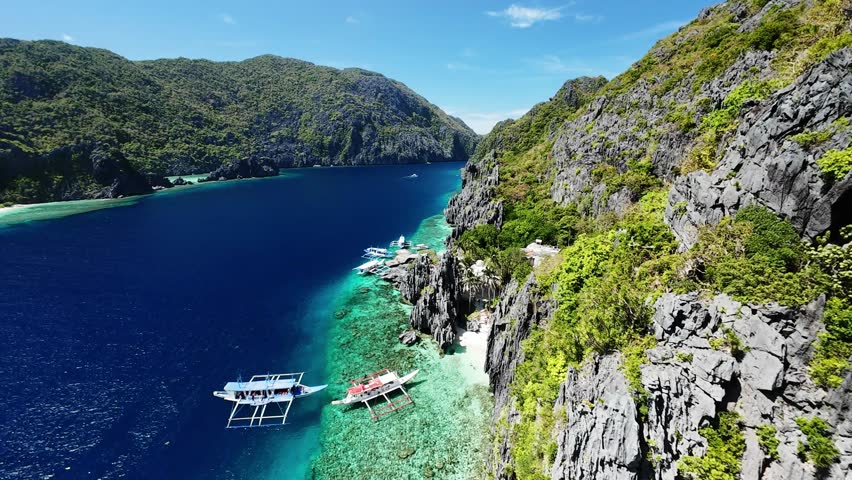 Aerial view of boats anchored by cliffs in El Nido, Palawan with clear blue water and tropical scenery