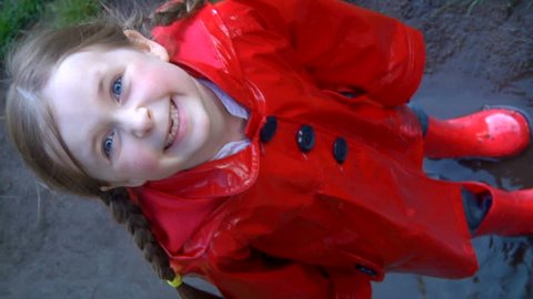 Splashing in a puddle - A child in red wellington boots jumps into a puddle and then smiles at the camera
