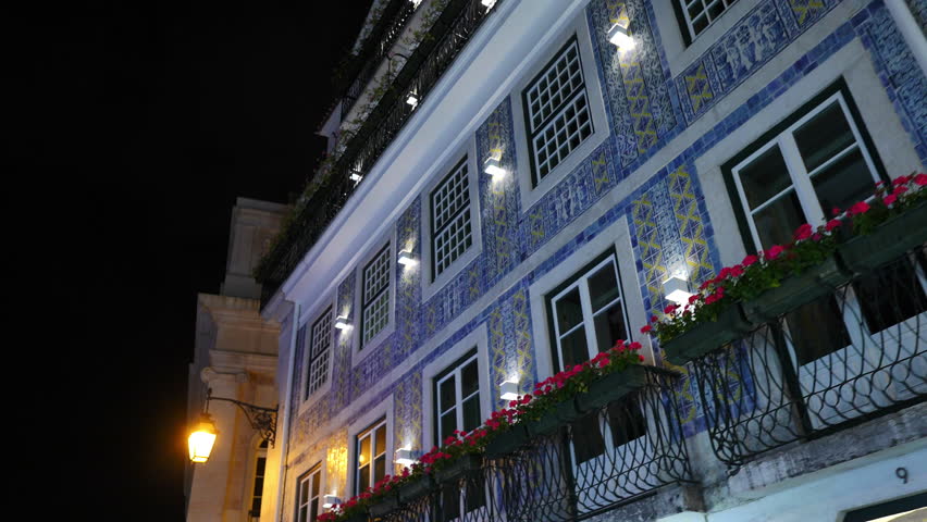 Vibrant blue and yellow ceramic azulejos adorning Portuguese building facade, glowing under nighttime illumination in historic Lisbon streetscape