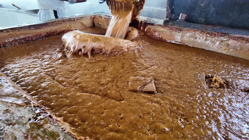 Traditional Sugar Cane Processing: Man Scooping Hot Juice