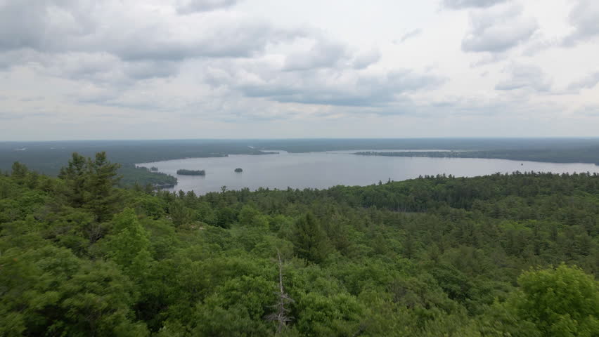 Aerial shot over green tree covered mountain on to large lake on cloudy day. Calabogie Ski hill. Ontario Canada