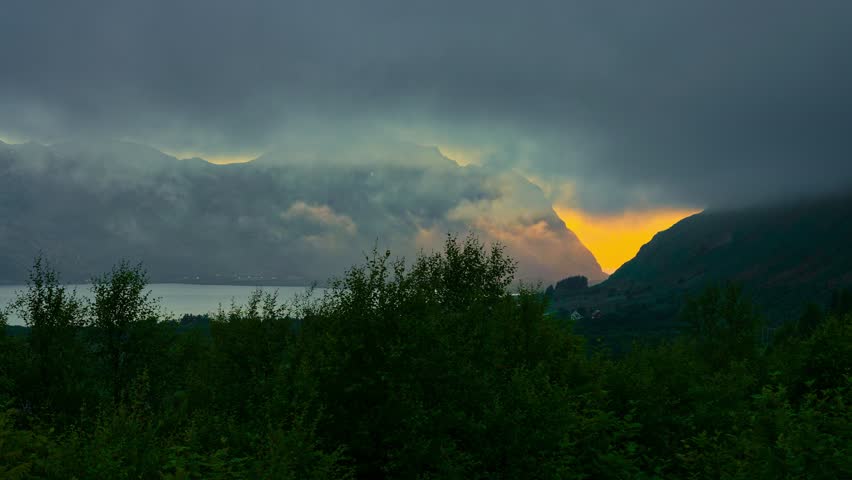 Thick Fog Time Lapse. Heavy sea mist covering up the view of fjord where midnight sun shining between the mountains. Lofoten islands, Northern Norway.