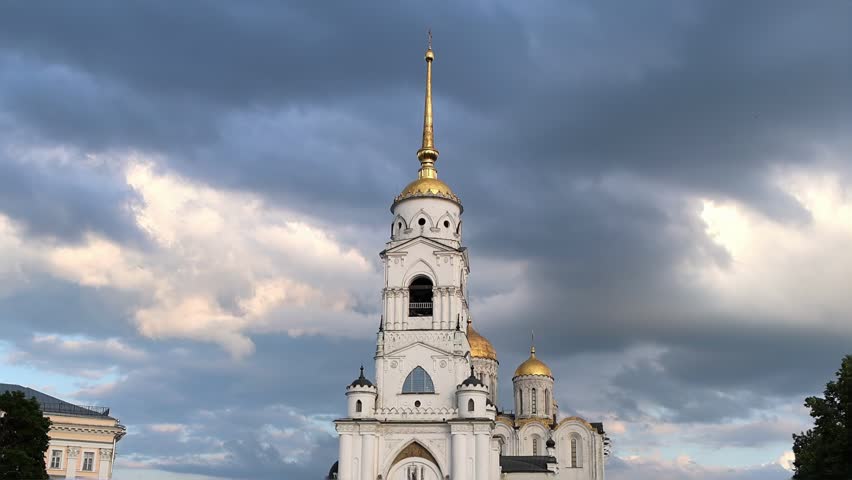 Majestic Orthodox cathedral in Vladimir with golden domes stands tall under dramatic evening sky. White stone architecture contrasts beautifully with stormy clouds above. Historic spiritual landmark