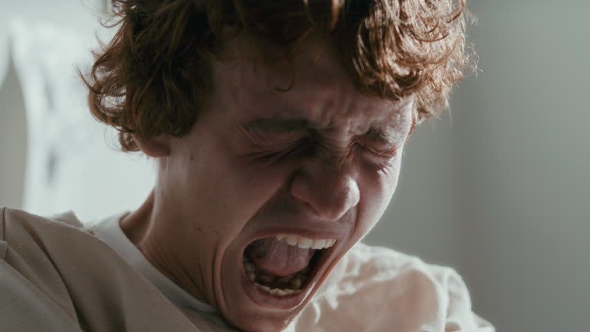 Frustrated male patient in straitjacket screaming during emotional breakdown in psychiatric hospital ward. Close-up view