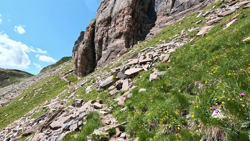 Narrow Hiking Trail Winding Along Rocky Alpine Slope with Sheer Cliffs and Blue Sky in the Italian Alps