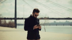 modern man with a beard and sunglasses checks his smartphone outdoors representing connectivity and urban lifestyle. Digital communication smartphone using. Remote work contemporary life - Powered by Shutterstock - Get 15% off with code: PIKWIZARD15