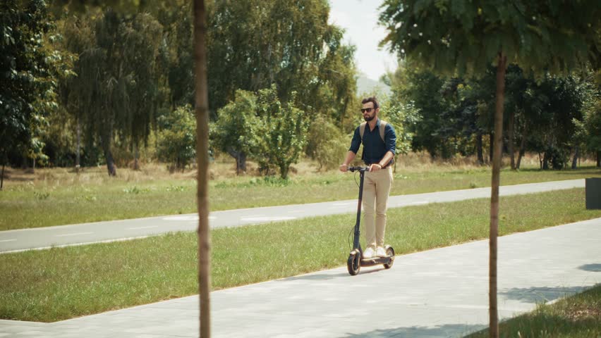 Commuter stylish man ride electric scooter in sunny park embodying modern urban mobility outdoor leisure. Personal transport electric scooter. Urban mobility commuting transport. Sustainable transport