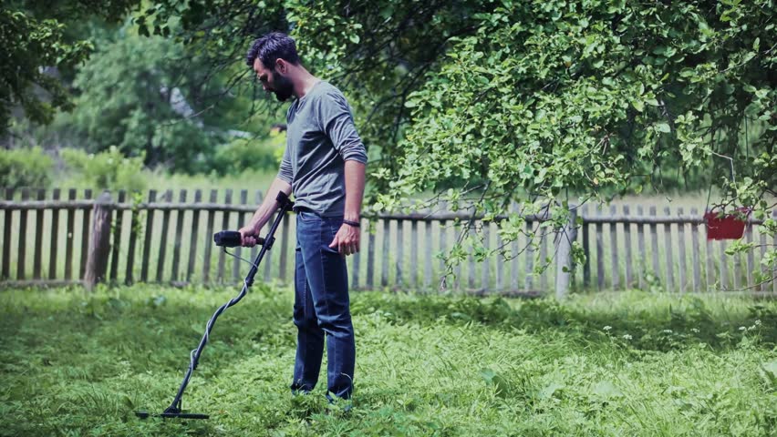 man diligently uses a metal detector in a lush green backyard or field, searching for hidden treasures or forgotten artifacts, highlighting hobbies, exploration, and outdoor activity. Archeology hobby
