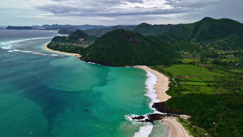 Breathtaking Kuta Beach with lush green mountains and clear turquoise water in Bali.
