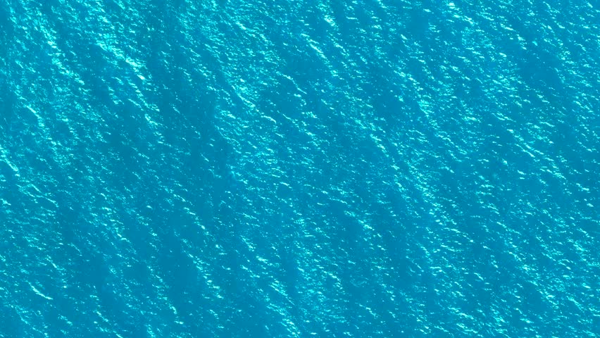 Aerial video of blue sea water background and sun reflection. Drone flight over turquoise water surface in open ocean. Flying over sea from above. Sea sunrise, ripples of ocean waves.
