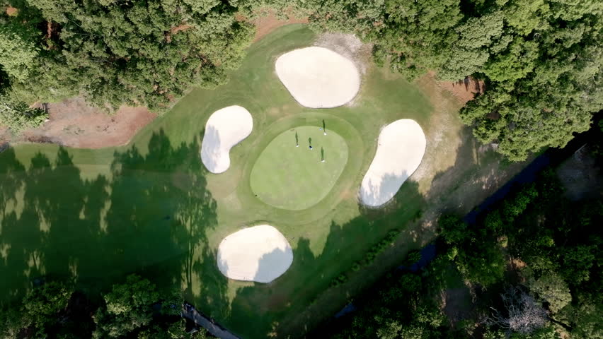 Aerial view of a lush golf green surrounded by four sand bunkers and trees, capturing Hilton Head’s scenic and refined golfing landscapes.