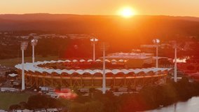Drone glides over a large sports stadium at sunset, capturing dramatic lighting, illuminated field lights, and the adjacent river in Gold Coast, Australia - Powered by Shutterstock - Get 15% off with code: PIKWIZARD15
