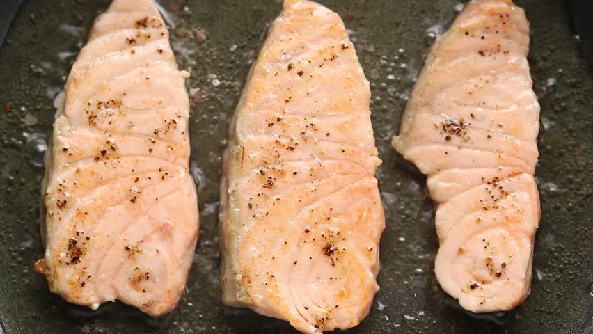 Pan-fried sliced salmon fillet on hot pan. Top view
