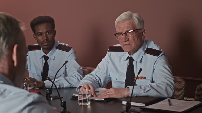 Medium shot of intercultural uniformed military delegates shaking hands while sitting at table during formal meeting indoors