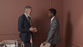 Medium long shot of two intercultural delegates in formal suits communicating during break in office, copy space - Powered by Shutterstock - Get 15% off with code: PIKWIZARD15