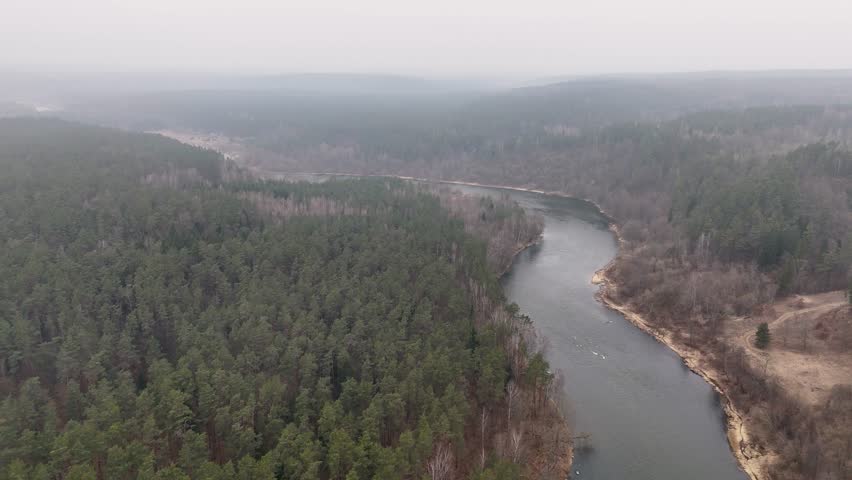 Aerial view of a winding river flowing through a dense forest in a misty landscape.