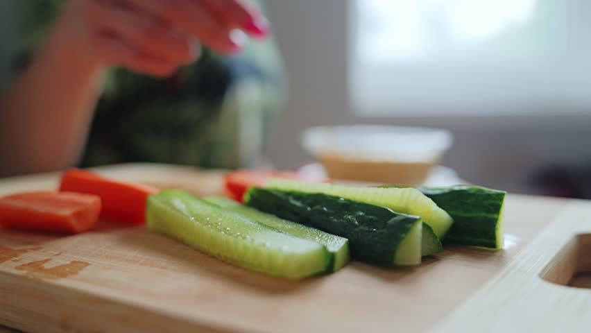 Close up slow motion of woman with pink nails dipping cucumber into hummus