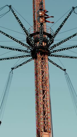 Spinning carnival swing ride rotating high above colorful fairground, chairs moving against bright blue summer sky during festive entertainment moment
