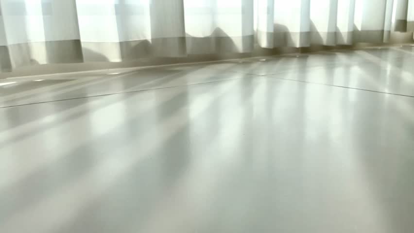 Sunlight through sheer curtains casts soft, shifting shadows on a polished concrete floor, creating a tranquil, minimalist indoor light - play scene.