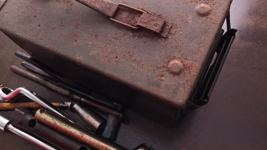A hand reaches into a metal toolbox, sorting through various wrenches, sockets, and other tools. Close-up shot, focusing on the tools and hand movement.