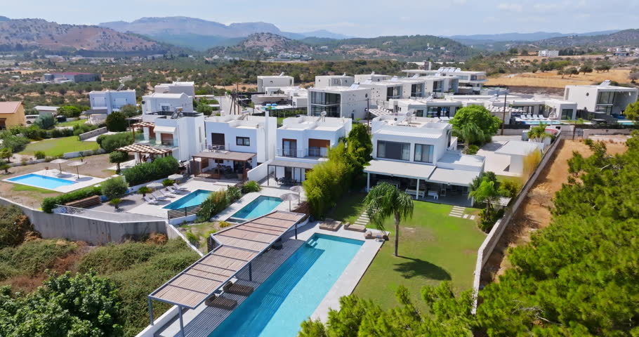 Drone flying in front of upscale vacation homes on a hill, in sunny Rhodes, Greece