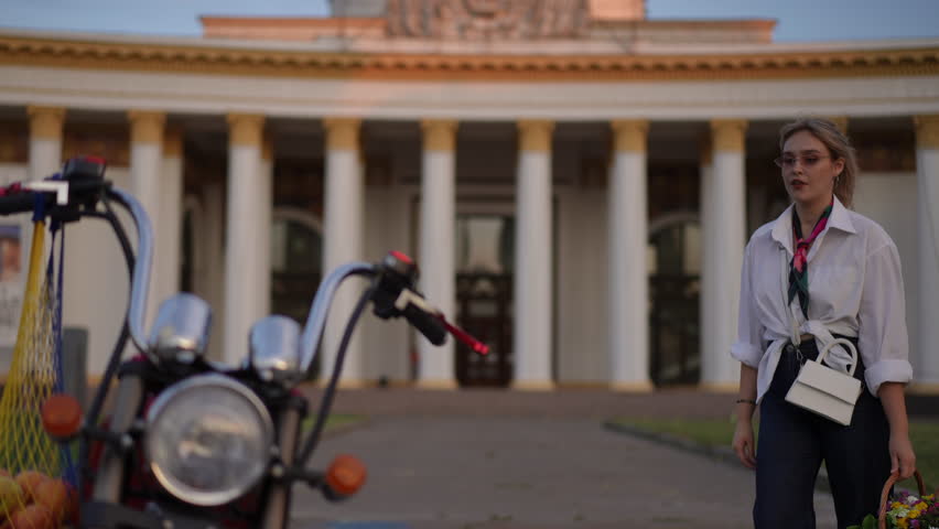 A stylish woman joyfully interacts with her beautiful motorcycle, adorned with a lovely flower basket