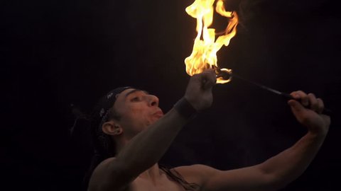 Young man firebreathing against black background - super slow motion
