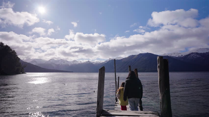 A mother and daughter stroll along a rustic wooden pier overlooking Lago Traful in Argentina.