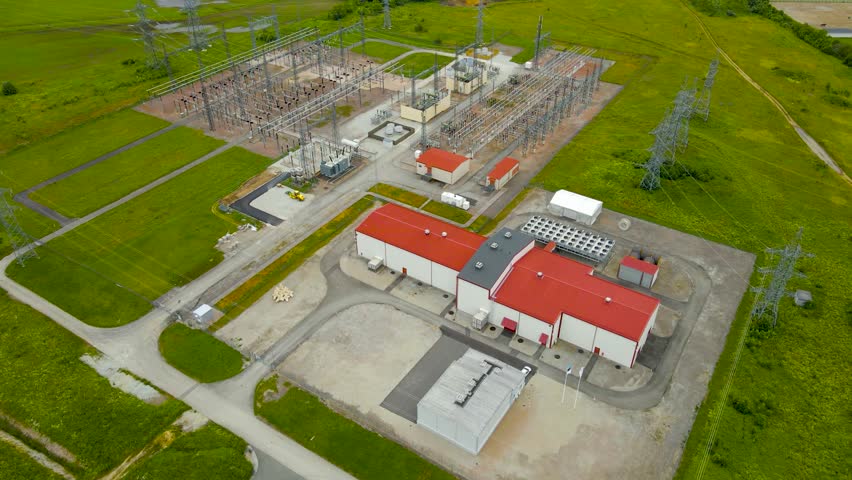 Aerial pull out revealing drone footage of a electrical substation and its control room or a data centre that has lots of electrical lines and cables visible during a summer cloudy day. Power station.