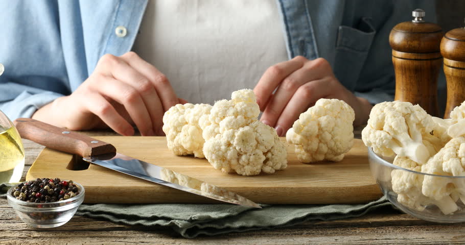 Woman cutting raw cauliflower at wooden table, closeup