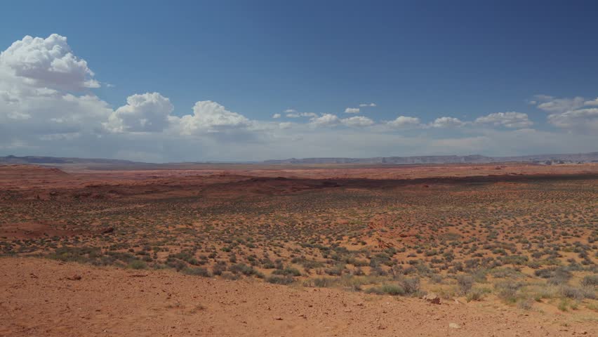 Vast desert landscape with scattered shrubs under a blue sky filled with fluffy clouds, captured in the American Southwest.
