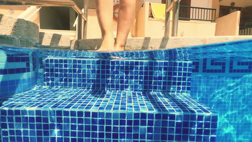 Gopro - underwater shot underwater view of woman wearing orange bikini, walking down pool steps with blue mosaic tiles surrounding, embodying summer relaxation