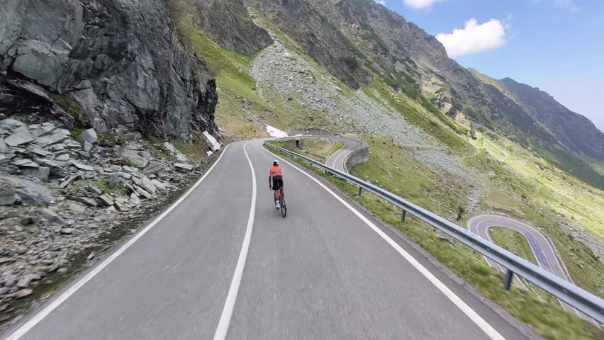Epic shot of a cyclist conquering a challenging mountain road. Stunning scenery with winding asphalt road, rocky slopes, and glimpses of snow. Perfect for adventure, travel, and sports themes.