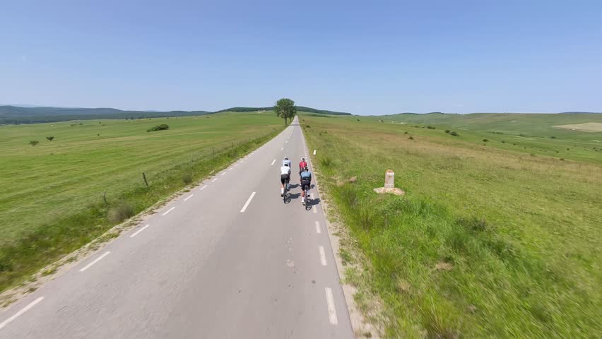 Four cyclists ride in formation down a long, straight road.The vast green fields under a clear blue sky create a sense of freedom and adventure.Perfect for travel, sports,and active lifestyle projects