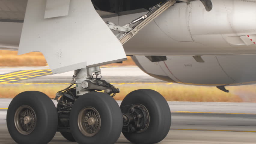 Close-up view of a commercial aircraft engine and landing gear on the tarmac. Themes of travel, transportation, maintenance, and modern aviation