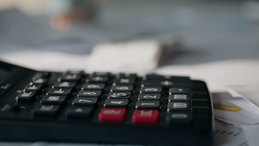 Fingers pushing calculator buttons at cabinet table full of documents closeup. Unknown man typing counting machine working. Entrepreneur hands calculating budget. Financial bills and business concept - Powered by Shutterstock - Get 15% off with code: PIKWIZARD15