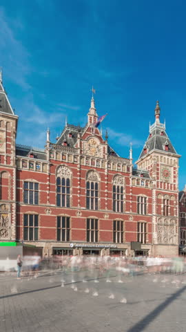 Hyperlapse of Amsterdam Central Railway Station with a historic building entrance. Many passengers moving in and out timelapse. Clouds in a blue sky. Amsterdam, The Netherlands