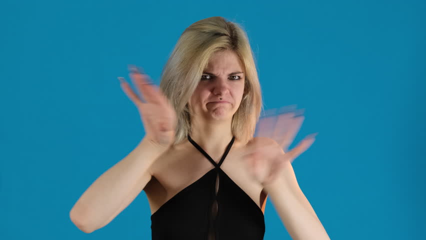 Woman displays thumbs-down gesture on blue background. Blonde lady clearly expressing displeasure and dissatisfaction with situation or object