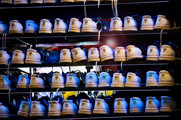 Zooming at a rack with bowling shoes, many different sizes. Blue atmospheric light. Slow motion. Modern bowling alley reception design